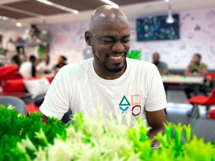 一个人穿着印有几何图案的白衬衫，坐在一张桌子旁，周围是生机勃勃的绿色植物，咖啡馆里一片生机勃勃的景象。