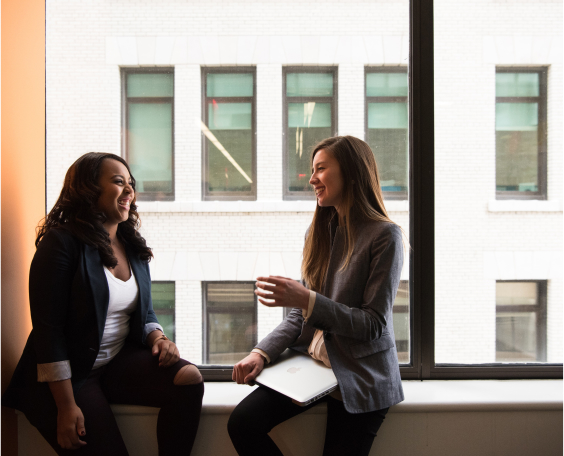 Two female colleagues chatting and smiling in an office environment