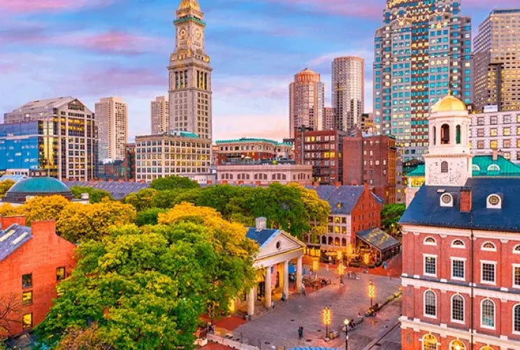 Sunset over Boston, Massachusetts, casting warm hues across the skyline and reflecting on the water.