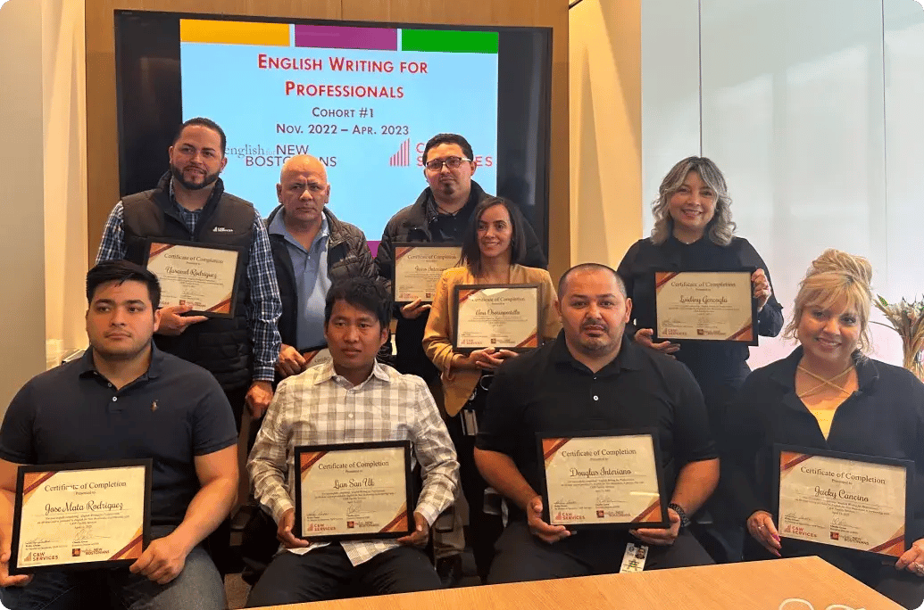 Group photo of participants holding completion certificates for the "English Writing for Professionals" course, with a presentation screen in the background.