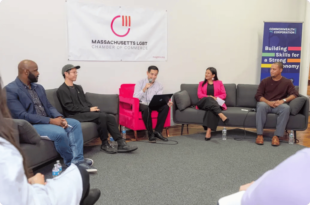 Panel discussion at the Massachusetts LGBT Chamber of Commerce with speakers seated on a gray couch, featuring topics on economic skills and diversity.