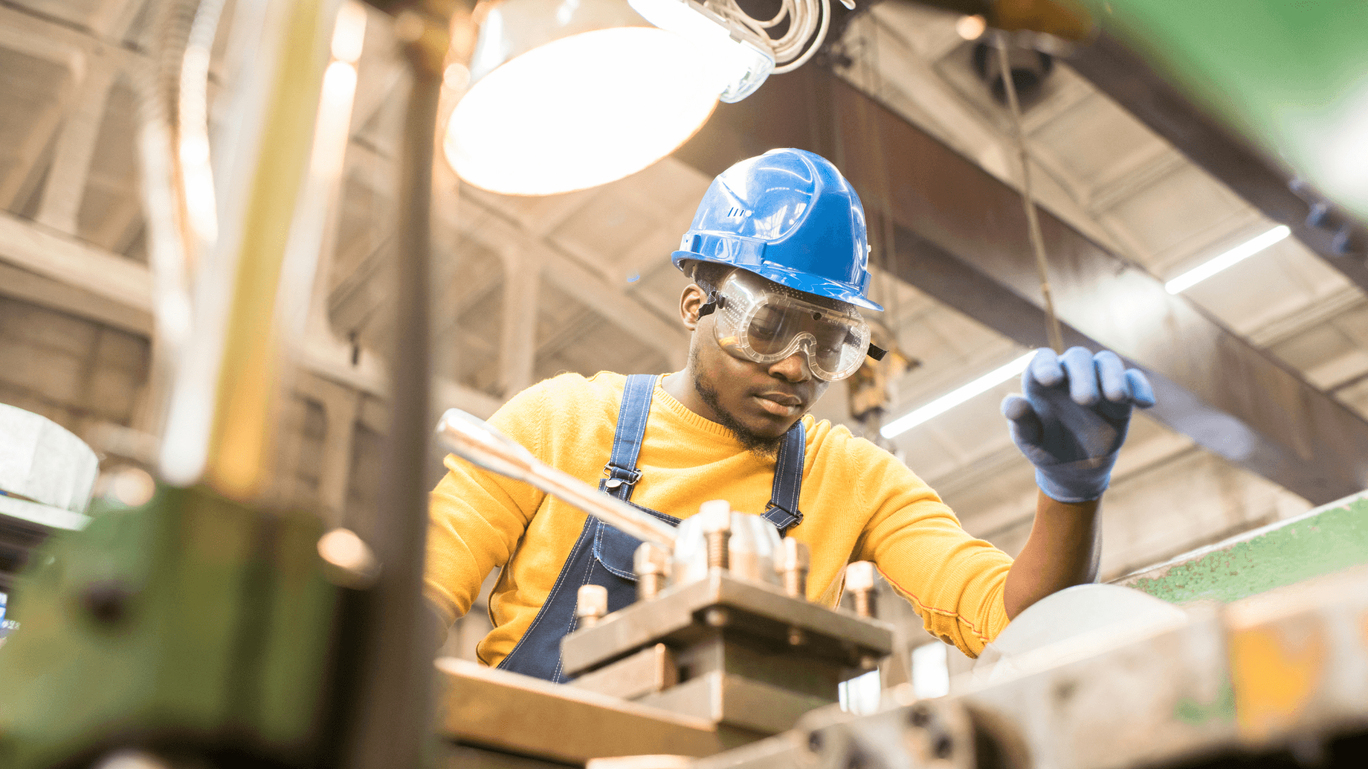 A man in a yellow shirt and hard hat operates a machine, focused on his task in a work environment.